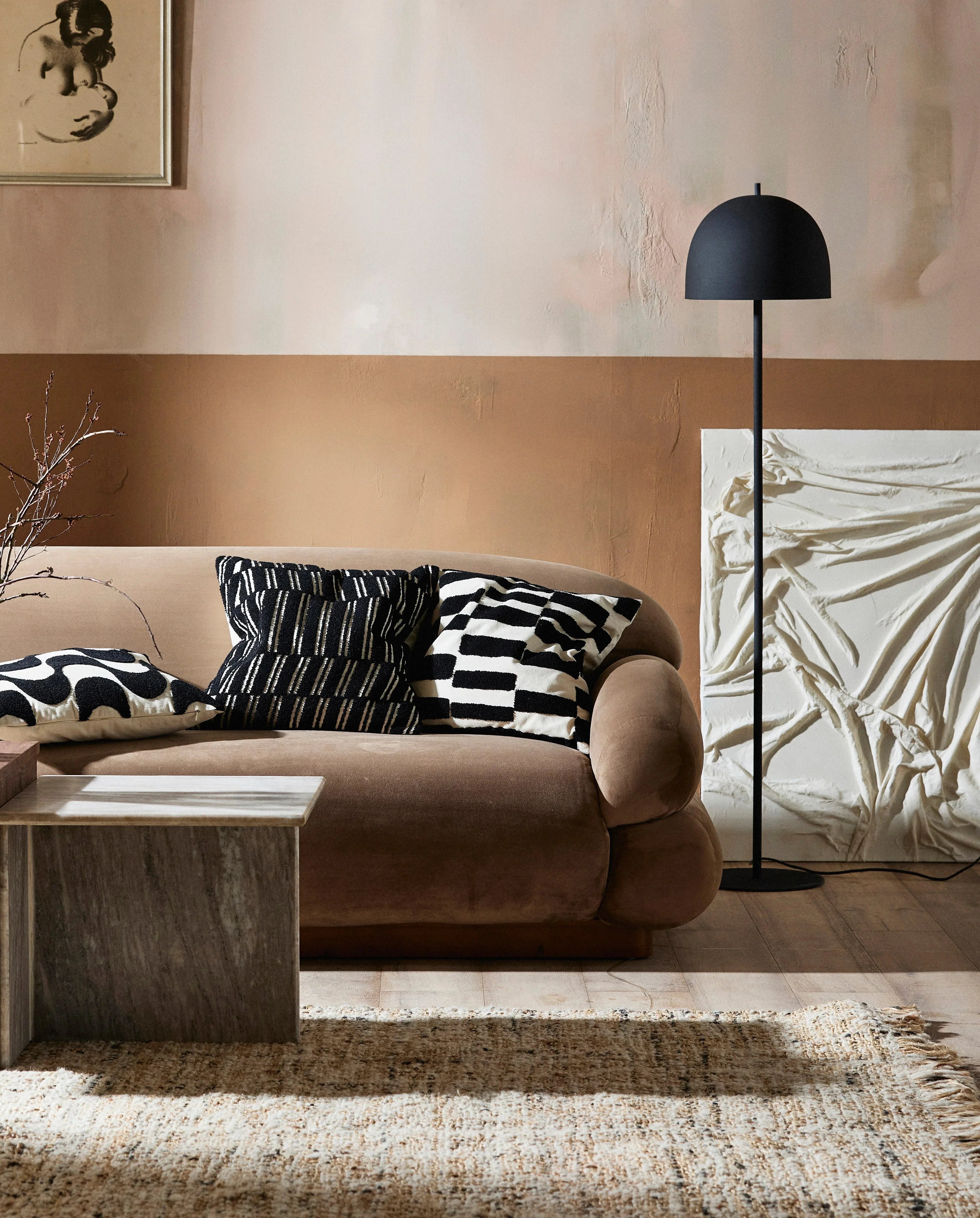 Brown velvet sofa with black and white geometric pillows, modern floor lamp, and textured rug in stylish living room