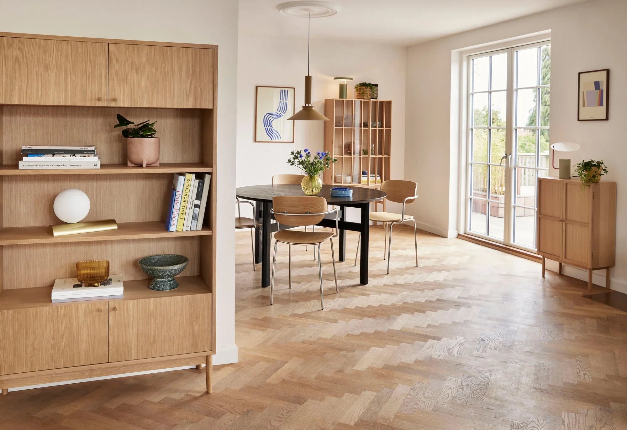 Modern dining room with wooden herringbone floor, black round table, wooden chairs, and natural light