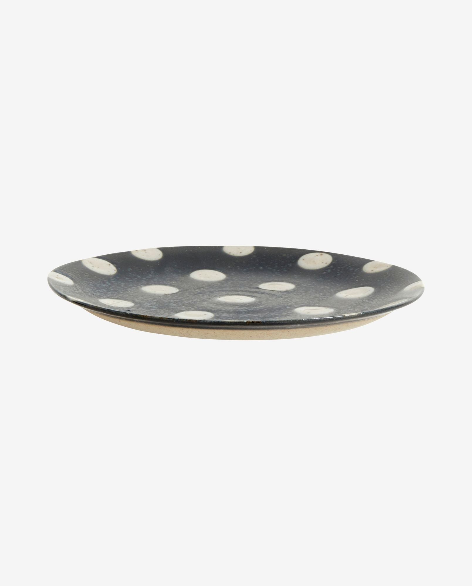 Black ceramic plate with white polka dots and a beige underside on white background